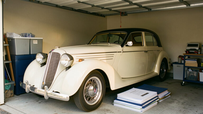 Automobile ancienne restaurée dans un garage privé propre et sécurisé, entourée de dossiers vierges, de clés et de matériel de rangement.